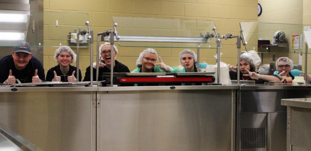 Members Will McKenna, Kirsten Pettit, Bri Dulin, Abby McKenna, Addi Obadal, Aden Dawson-Fink, and Zane Helter pose in between serving meals. . Click to read article